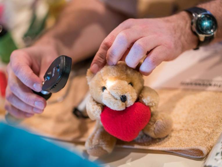 Ein kleiner Teddybär mit rotem Herz im Arm wird von einem Tierarzt untersucht.